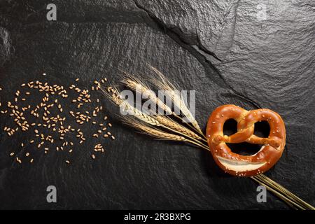 Brezel neben Getreideohren und Getreidekörnern Stockfoto