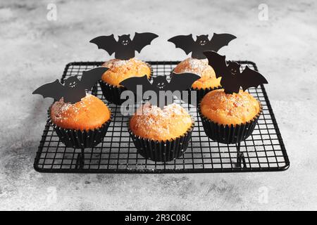 Halloween-Kürbis-Muffins in schwarzen Kapseln, dekoriert mit Fledermäusen aus Pappe. Festlicher Halloween-Cupcake Stockfoto