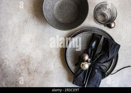 Minimalistische Tischeinstellung mit schwarzem Steingut und Weihnachtsdekoration auf grauem Betonhintergrund Stockfoto
