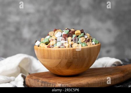 Bunte Schokoladensteine. Schokoladendragee aus Stein in Holzschüssel auf dunklem Hintergrund. Kleine mehrfarbige Süßigkeiten Stockfoto