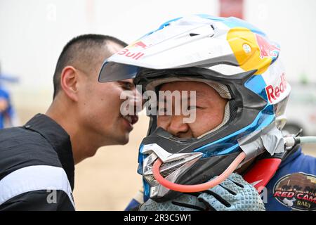 Maigaiti, Chinas autonome Region Xinjiang Uygur. 23. Mai 2023. Der Motorradfahrer Wang Yun wird von einem Mitarbeiter seines Teams nach Abschluss der dritten Etappe in der Wüste von Maigaiti County bei der Taklimakan Rally 2023, der Autonomen Region Xinjiang Uygur im Nordwesten Chinas, am 23. Mai 2023 beglückwünscht. Kredit: Hu Huhu/Xinhua/Alamy Live News Stockfoto