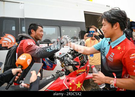 Maigaiti, Chinas autonome Region Xinjiang Uygur. 23. Mai 2023. Der Motorradfahrer Fang Mingji (L) schüttelt sich mit seinem Sohn Fang Xiangliang (R), der auch sein Teamkollege ist, die Hand, nachdem er die dritte Etappe in der Wüste von Maigaiti County bei der Taklimakan Rally 2023, der Autonomen Region Xinjiang Uygur im Nordwesten Chinas, am 23. Mai 2023 beendet hat. Kredit: Hu Huhu/Xinhua/Alamy Live News Stockfoto