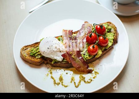 Getoastetes Brot mit Avocado, Speck, pochiertem Ei und Tomaten Stockfoto