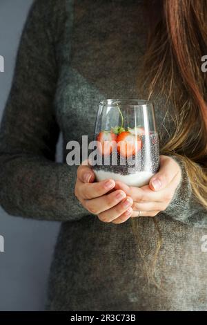 Eine Frau, die Glas mit Chia-Pudding und Joghurt mit Erdbeeren hält Stockfoto