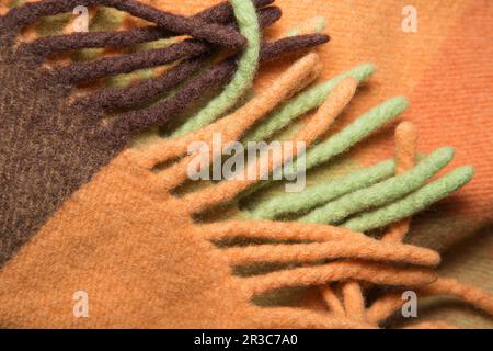 Weiche und warme gefaltete Alpakawolldecke mit Fransen. Makroshot mit karierter Struktur aus grüner und orangefarbener Wolle Stockfoto