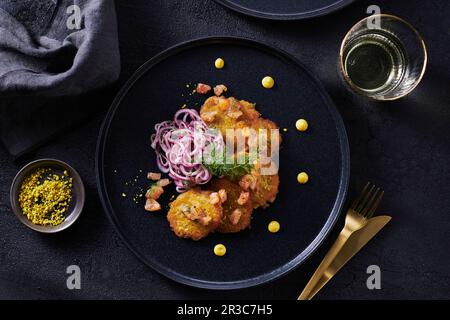 Kleine Lachskuchen mit Zwiebelsalat auf schwarzem Teller, mit goldenem Besteck Stockfoto