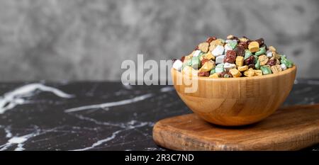 Bunte Schokoladensteine. Schokoladendragee aus Stein in Holzschüssel auf dunklem Hintergrund. Kleine mehrfarbige Süßigkeiten. Speicherplatz kopieren. Leerer Platz für te Stockfoto