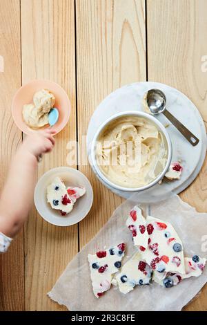 Obstsplitter und Eis für Kinder. Die Hand eines Kleinkindes greift mit einem Löffel hinein Stockfoto