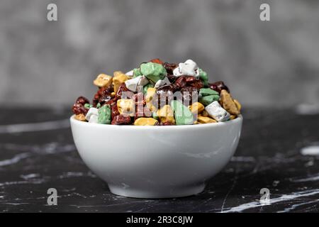 Bunte Schokoladensteine. Steinschokoladendragee in Keramikschüssel auf dunklem Hintergrund. Kleine mehrfarbige Süßigkeiten Stockfoto