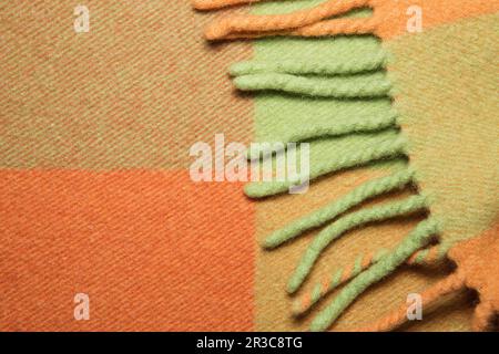 Weiche und warme gefaltete Alpakawolldecke mit Fransen. Makroshot mit karierter Struktur aus grüner und orangefarbener Wolle Stockfoto