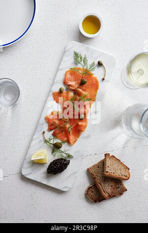 Geräucherter Lachs mit Kapernäpfeln auf einer Servierplatte aus Marmor Stockfoto
