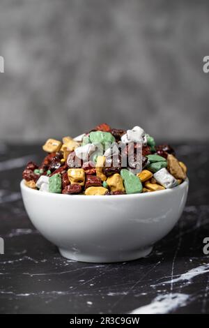 Bunte Schokoladensteine. Steinschokoladendragee in Keramikschüssel auf dunklem Hintergrund. Kleine mehrfarbige Süßigkeiten Stockfoto