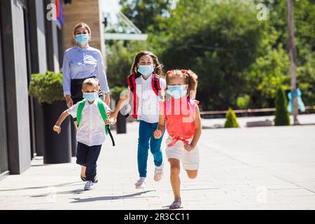 Die Schulkinder mit medizinischen Masken verlassen die Schule Stockfoto