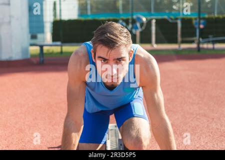 Fokussierter junger, männlicher, kaukasischer Sportler, bereit für das Laufrennen in einer Sprint-Ausgangsposition Stockfoto