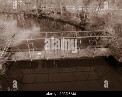 Eine Reise durch die Zeit in Sepiatönen: Eine alternde Brücke über einen ruhigen Fluss, umgeben von warmen Farbtönen, ruft Nostalgie und ein zeitloses Gefühl der Geschichte hervor. Stockfoto