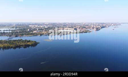 Die Drohne fliegt über den gewundenen Fluss, umgeben von einer Industriestadt mit verschiedenen Gebäuden und Feuchtgebiet und mar Stockfoto