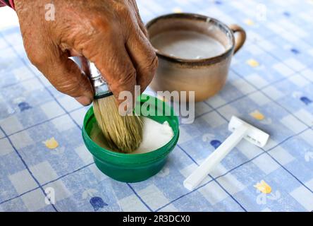 Ältere Hände mit Rasierbürste und Klinge auf blauem Tisch Stockfoto
