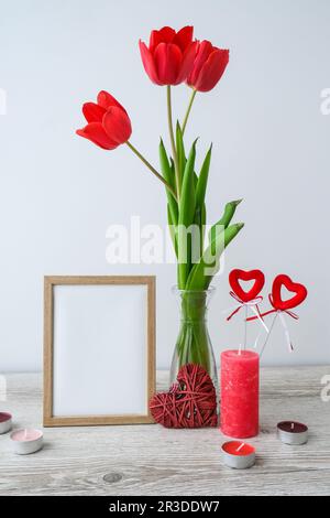 Weihnachtsmodell. Tulpenblüten in Glasvase mit Bilderrahmen an Holztisch-Hintergrundwand zu Hause, Nahaufnahme, Mütter Stockfoto