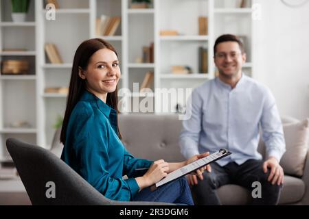 Portrait eines professionellen Psychologen konsultiert einen männlichen Patienten in einem Zustand von Stress und Depression, der auf dem Sofa im Büro sitzt. Sie schreibt drauf Stockfoto