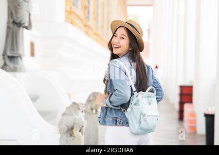 Porträt einer asiatischen Reisenden, die auf dem Fußweg des Tempels spaziert, während sie zurück in Bangkok, Thailand, Südostasien lächelt - eine Frau, die allein mit dem Rucksack unterwegs ist - mit Kopierbereich Stockfoto