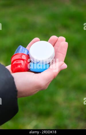 Nahaufnahme bei Weiblichen Händen voller farbenfroher Plastikbecher, eine Handvoll verschwendeter Plastikdeckel. Recycling. Sammeln Stockfoto