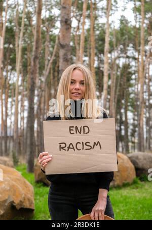 Porträt einer weissen jungen Frau im Hut mit Pappe und Text im Freien. Naturhintergrund. Protestaktivist Stockfoto