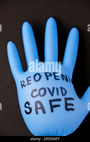 Aufgeblasener blauer Latex-OP-Handschuh auf schwarzem Hintergrund. - Ich öffne den Covid-Safe wieder. Öffnen Sie wieder Text auf medizinischen Handschuhen. Neue Norm Stockfoto