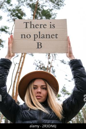 Porträt einer jungen weißhäutigen Frau mit Hut, die Pappe mit Text in der Hand hält. ES GIBT KEINEN PLANETEN B im Freien. Naturhintergrund. Demonstranten Stockfoto