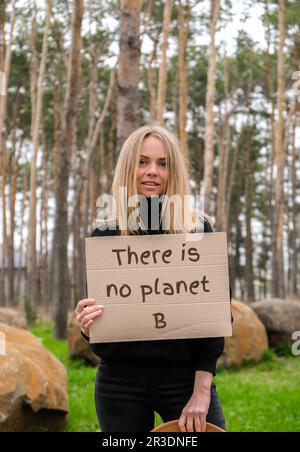 Porträt einer jungen weißhäutigen Frau mit Hut, die Pappe mit Text in der Hand hält. ES GIBT KEINEN PLANETEN B im Freien. Naturhintergrund. Demonstranten Stockfoto