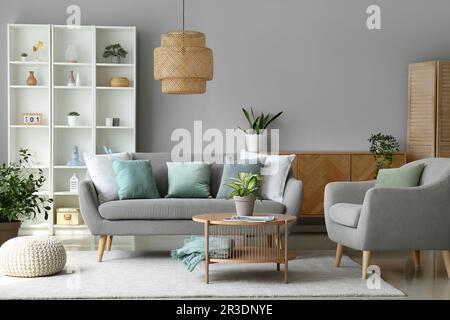 Stilvolles Wohnzimmer mit grauem Sofa, Sessel und Zimmerpflanzen auf dem Couchtisch Stockfoto