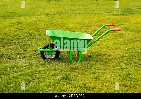 Ein grüner, eiserner, leerer Müllwagen steht auf dem grünen Gras, Stadtdienst Stockfoto