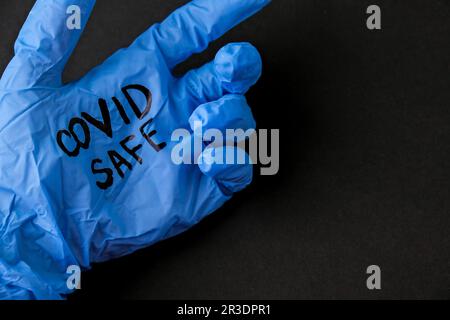 Aufgeblasener blauer Latex-OP-Handschuh auf schwarzem Hintergrund. - Ich öffne den Covid-Safe wieder. Öffnen Sie wieder Text auf medizinischen Handschuhen. Neue Norm Stockfoto