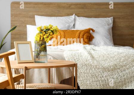 Vase mit Mimosablumen und Rahmen auf dem Tisch im Schlafzimmer Stockfoto
