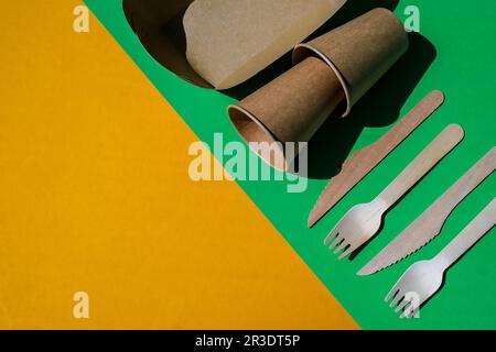 Holzgabeln und Pappbecher mit Platten auf farbigem Hintergrund. Umweltfreundliches Einweg-Geschirr. Verwendet in Fast Food, Restaurants, Stockfoto