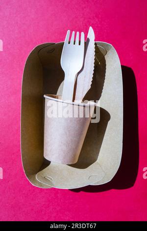 Holzgabeln und Pappbecher mit Platten auf farbigem Hintergrund. Umweltfreundliches Einweg-Geschirr. Verwendet in Fast Food, Restaurants, Stockfoto