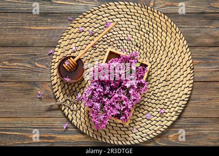 Korbmatte und Schachtel mit wunderschönen Fliederblumen mit Honig auf braunem Holzhintergrund Stockfoto