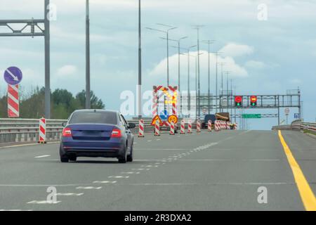 Straßenarbeiten, großes, helles mobiles Schild mit Streifen, Umleitungsrichtung. Das blaue Auto fährt auf eine freie Spur Stockfoto
