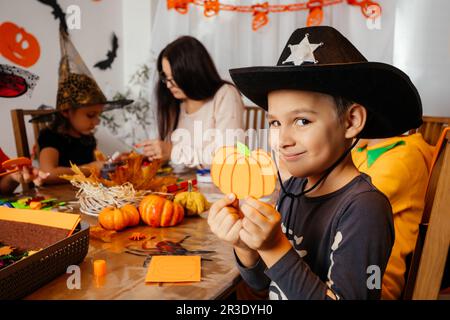 Niedlicher Junge im Cowboy-Hut zeigt seinen handgefertigten Papierkürbis Stockfoto