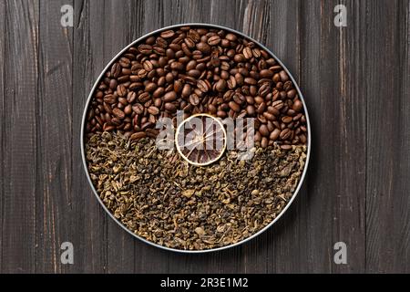 Grüner trockener Tee, Kaffeebohnen und ein Stück trockene Zitrone in einer runden Box auf dunklem Holzhintergrund von oben. Konzeptionelle Zusammensetzung von grünem Tee Stockfoto