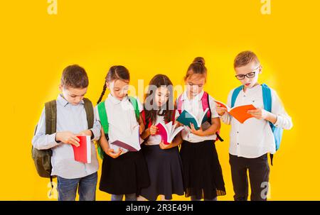 Fröhliche lächelnde kleine Studenten halten Farbbücher isoliert auf gelbem Hintergrund. Zurück zur Schule. Stockfoto