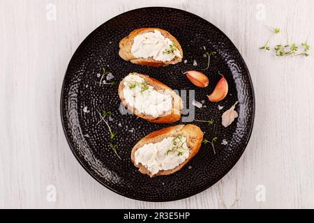 Baguettscheiben mit Knoblauchaufstrich auf schwarzem Teller. Stockfoto