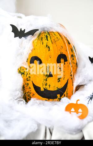 Kürbis mit gemaltem Gesicht auf farbigem Hintergrund für Halloween. Spinnennetz. Weihnachtsdekoration. Stockfoto