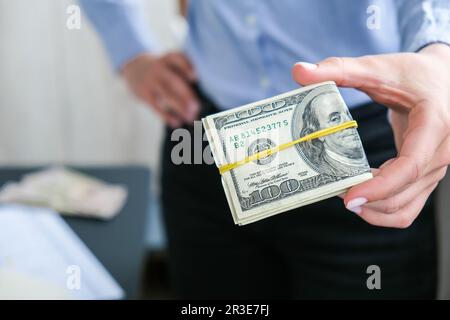 Eine Geschäftsfrau, die eine Menge Bargeld in US-Dollar zeigt. Nahaufnahme. Einkommen- und Geschäftskonzept. Vergeltung, Bestechung, Korruption Stockfoto