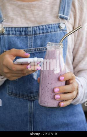 Weibliche Hände mit Blueberry Smoothie garniert mit Blaubeeren. Eine Frau, die ein Glas Frühstücksprotein-Smoothie trinkt. Verwenden Von Stockfoto