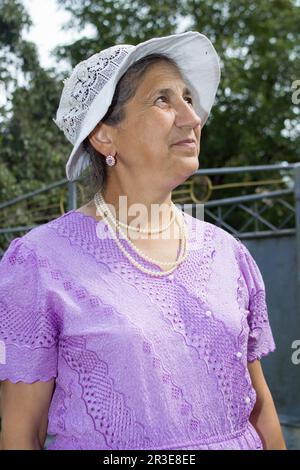 Ein Rentner mit weißem Hut und lila Kleid sieht in den Himmel Stockfoto