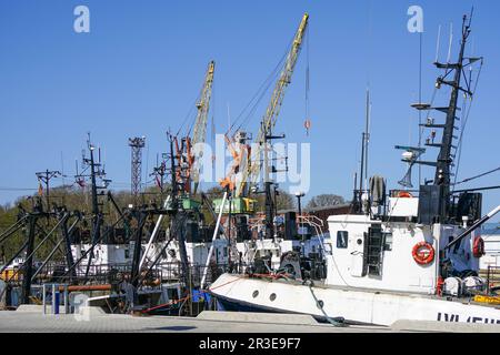 Farbenfroher Blick auf den Hafenpier mit kleinen Fischereifahrzeugen und Hafenkranen im blauen Hintergrund, Liepaja, Lettland, Ostsee Stockfoto