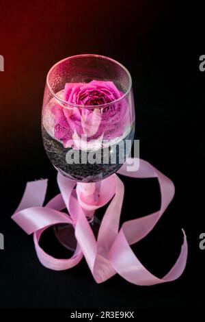 Weinglas gefüllt mit rosafarbenem Blumenpetalson-Tisch mit schwarzem. Minimales, modernes Stillleben. Urlaubskonzept Valentine oder Womans da Stockfoto