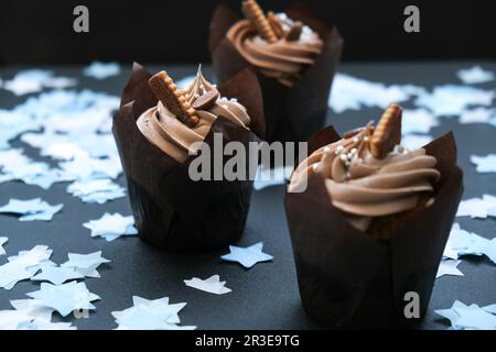 Köstliche Schokoladen-Cupcakes mit Sahne auf dunklem Hintergrund. Drei Schokoladen-Muffins. Geburtstagskuchenparty. Baby-Party für Jungen oder Mädchen Stockfoto