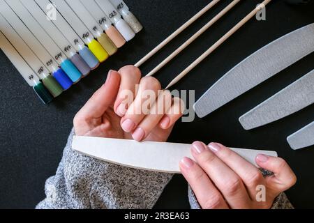 Arbeiten Sie zu Hause mit Nägeln. Nagelpflege, Selbstpflege. Weibliche Maniküre. Machen Sie die Maniküre alleine, während Sie zu Hause bleiben. Weibliche Hände und Stockfoto