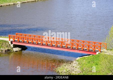 Eine kleine, wunderschöne orangefarbene Fußgängerbrücke über einen Fluss mit einem Stahlträger und Holzgeländern, einfache gerade Fußgängerbrücke Stockfoto